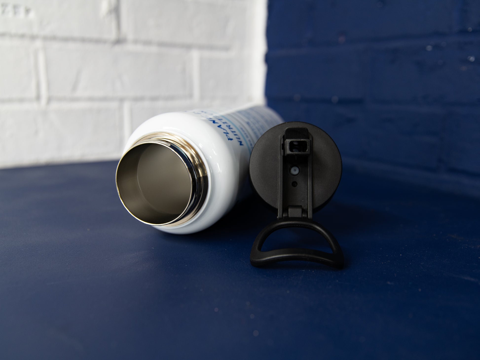 Wide-mouth stainless interior and flip-straw lid with carry handle shown beside the bottle.