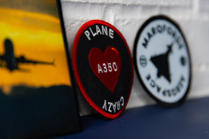 Close-up side view showing embroidered round “Plane Crazy A350” heart patch and Marqforde crest.