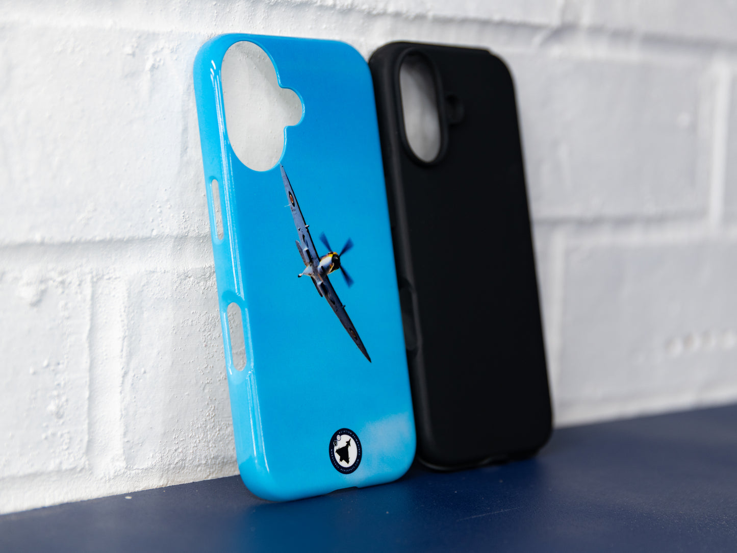 Front three-quarter view of blue Spitfire iPhone 16 tough case next to a plain black insert case.