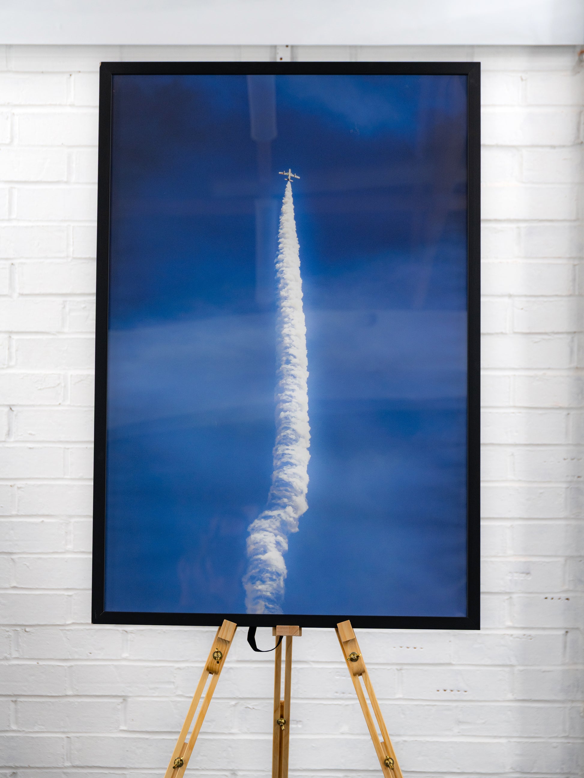 Straight-on view of the complete framed print with long white smoke trail and jet at the apex.