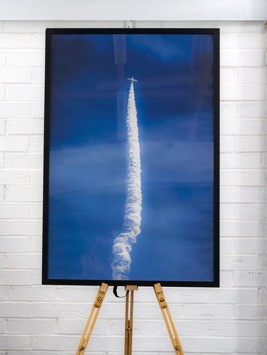 Straight-on view of the complete framed print with long white smoke trail and jet at the apex.