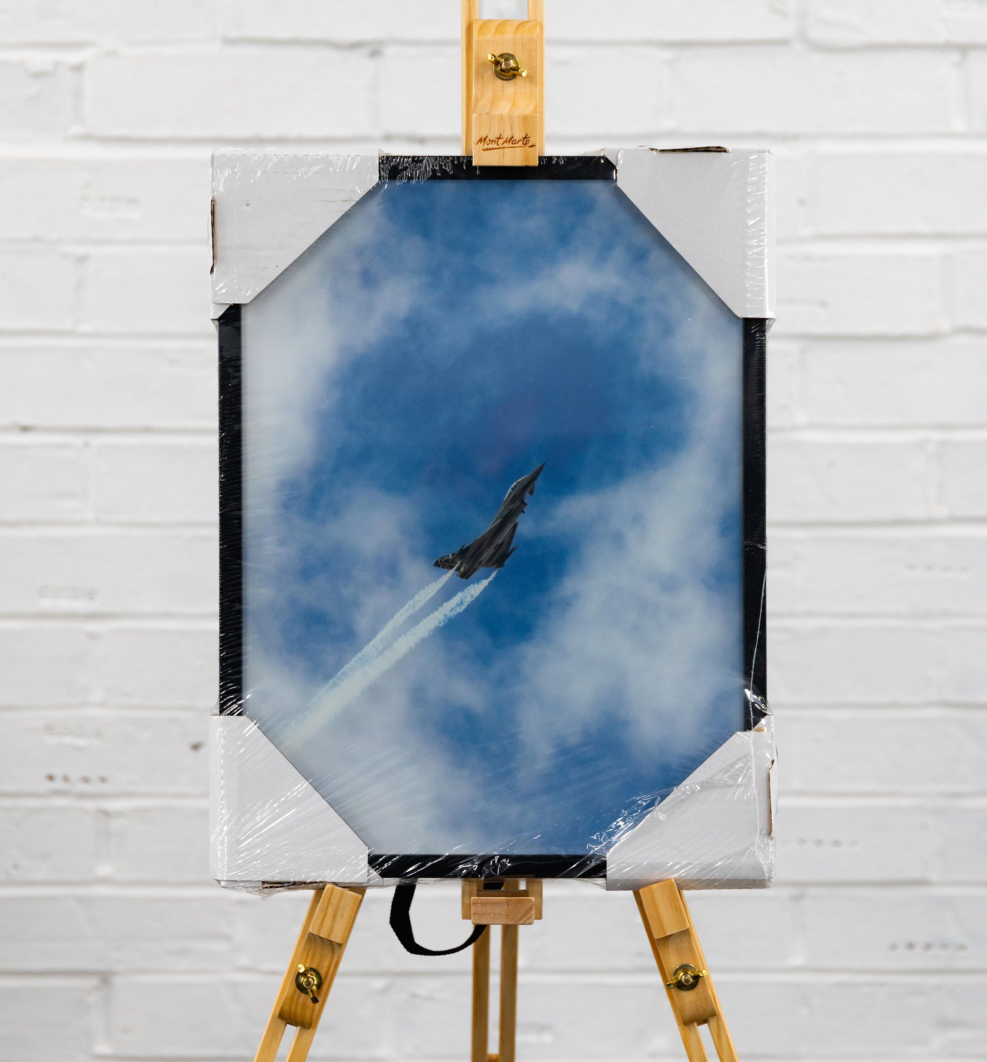 Front-on view of the framed print in factory wrap, showing the jet spearing up through blue sky and cloud