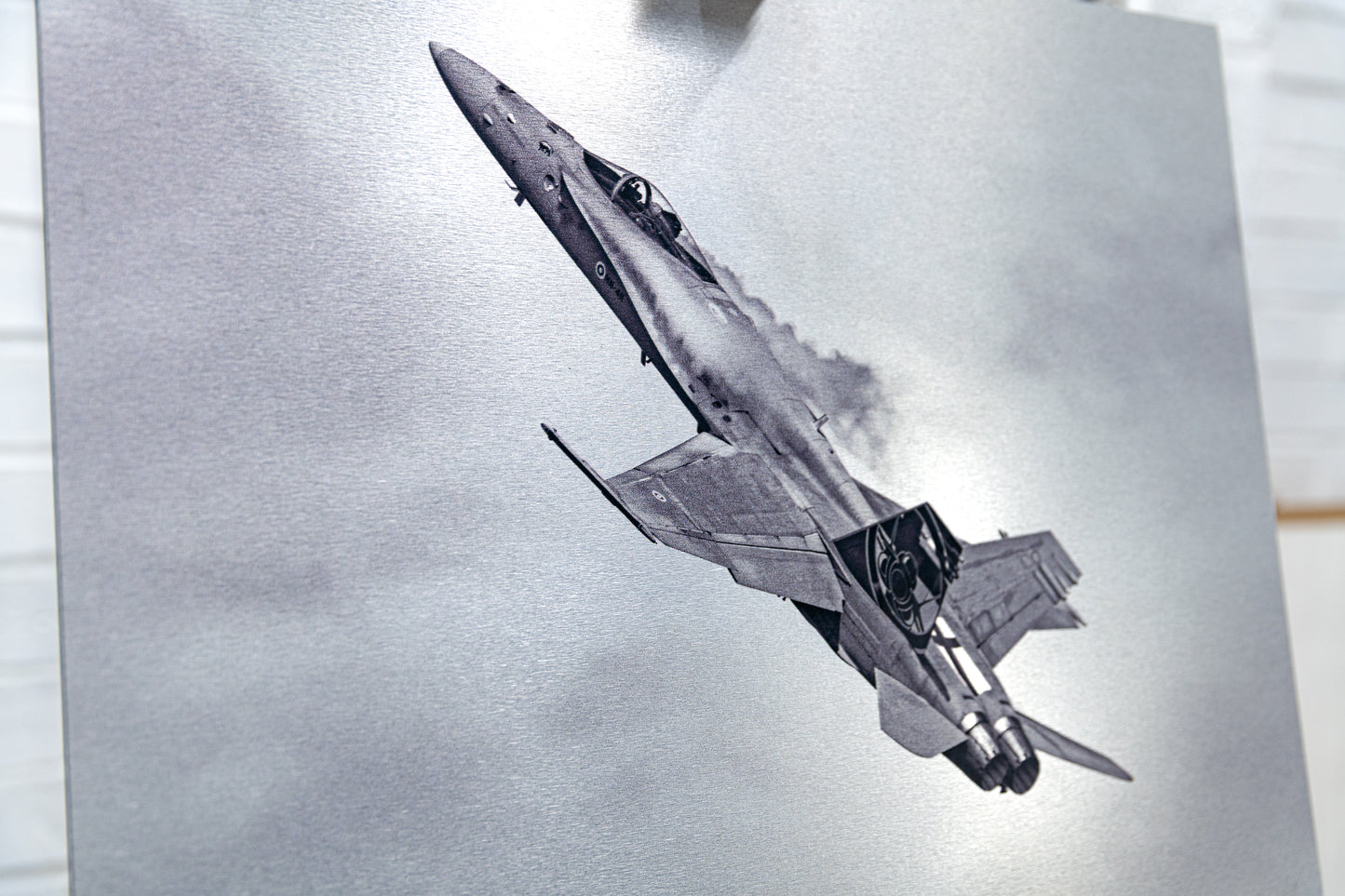 Angled detail of the brushed metal surface featuring a Finnish F/A-18 Hornet climbing with vapor trails