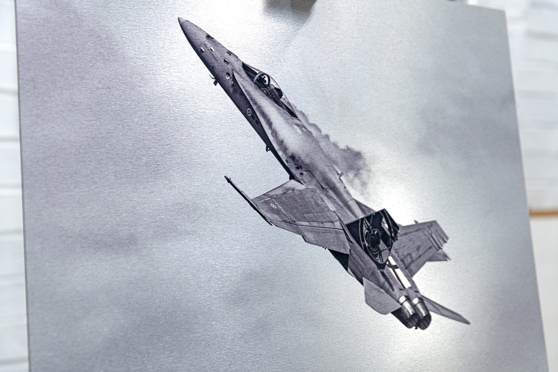 Angled detail of the brushed metal surface featuring a Finnish F/A-18 Hornet climbing with vapor trails