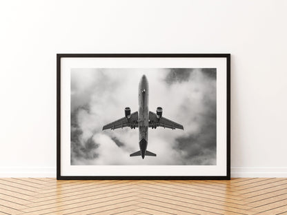 Airbus A320 passing directly overhead against bright cloud, black and white, aviation photo wall art print in a black frame