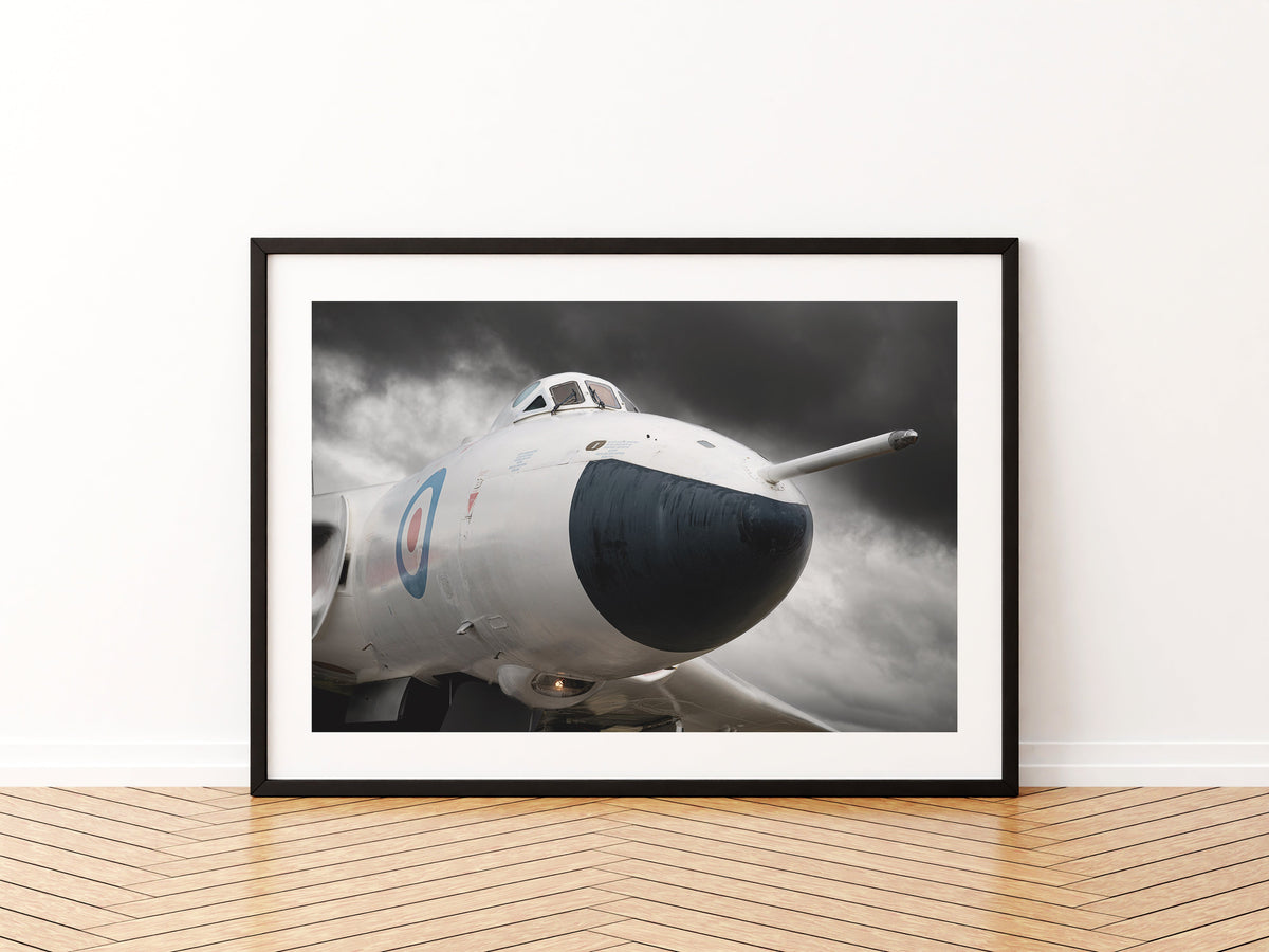 Nose of an anti-flash white Avro Vulcan bomber under a dark stormy sky, aviation photo wall art print in a black frame
