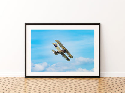 Sopwith Camel biplane climbing away against a blue sky with white cloud, aviation photo wall art print in a black frame