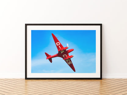 Red de Havilland DH88 Comet racer G-ACSS banking against a deep blue sky, aviation photo wall art print in a black frame