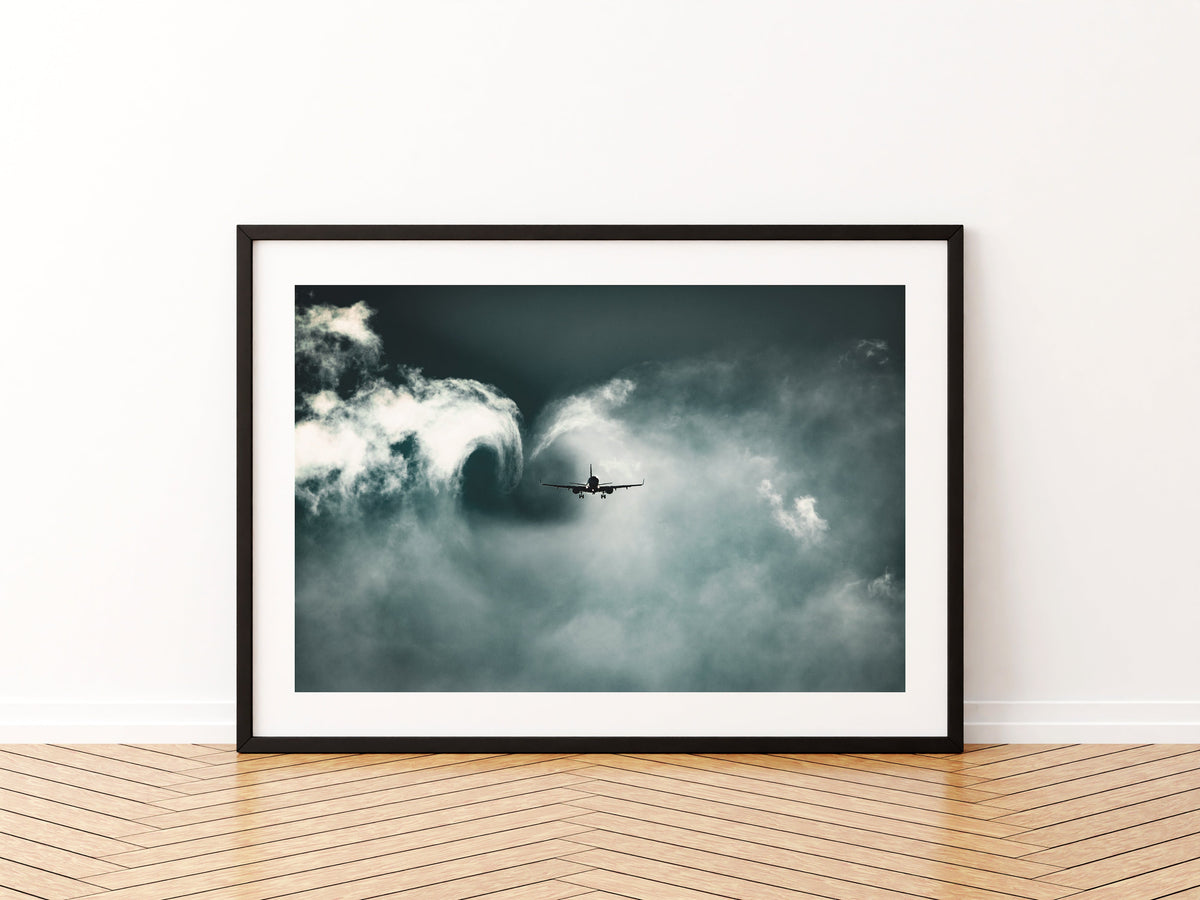 Airliner on approach carving a curling wake vortex through low cloud in teal light, aviation photo wall art print in a black frame