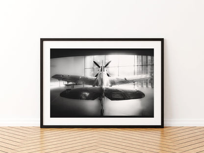Spitfire RW388 seen from behind, backlit by a gallery window, black and white, aviation photo wall art print in a black frame